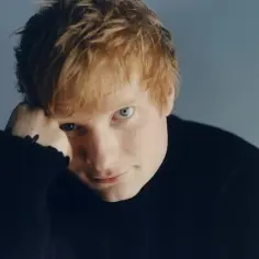 Ed Sheeran w czarnym golfie, opierający głowę na dłoni.