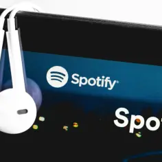 Białe słuchawki wiszą na ekranie smartfona z logo Spotify.